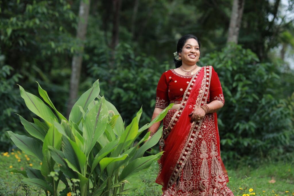 A woman in a red sari standing in front of plants